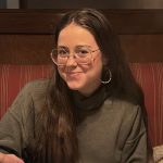 Woman with long brown hair and glasses smiles at the camera