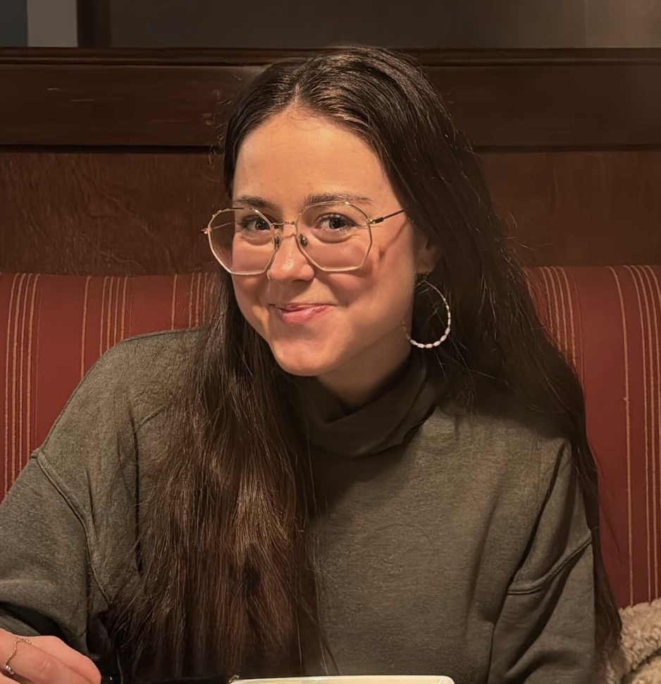 Woman with long brown hair and glasses smiles at the camera
