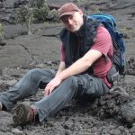 Björn Willige sitting on rocky lava-flow ground in hiking gear with backpack.
