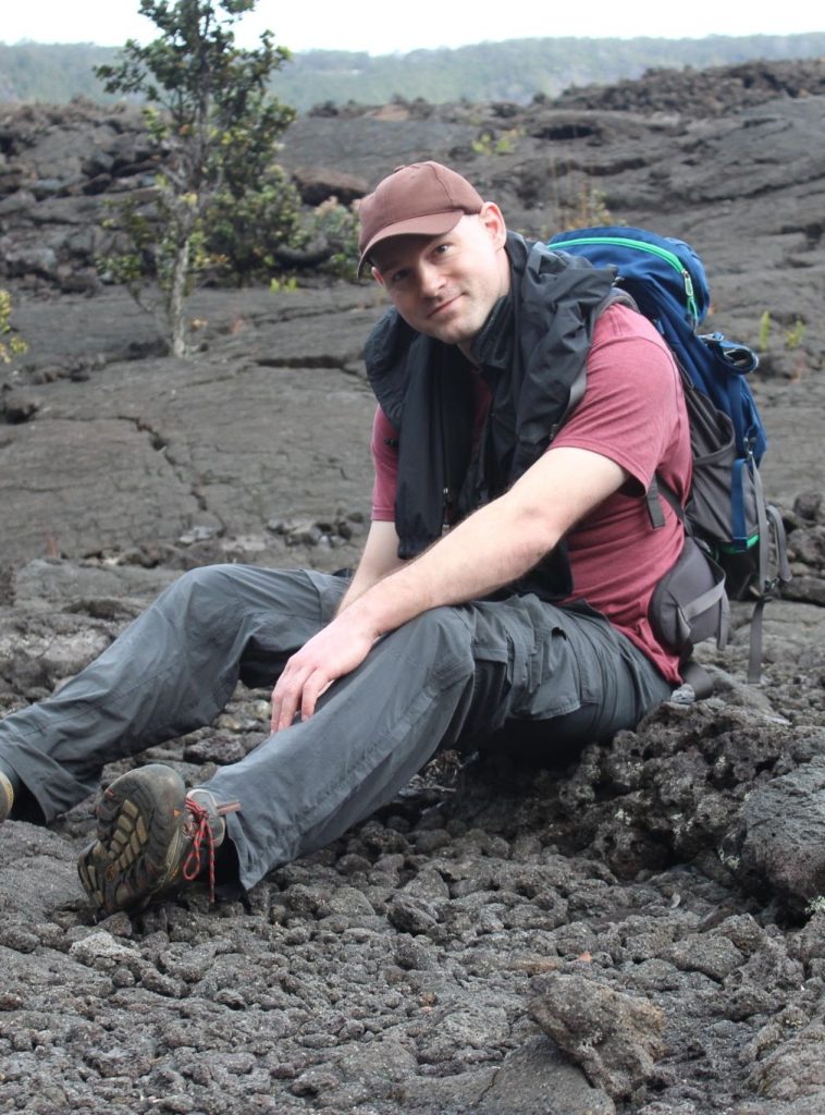 Björn Willige sitting on rocky lava-flow ground in hiking gear with backpack.