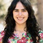 Headshot of Elizabeth Diaz-Clark in a colorful spring blouse with trees and sunlight in the background