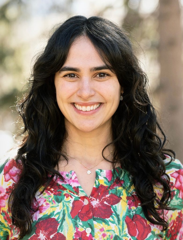 Headshot of Elizabeth Diaz-Clark in a colorful spring blouse with trees and sunlight in the background