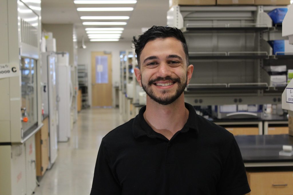Amir Alayoubi smiling at the camera while standing the CSU Biology lab.