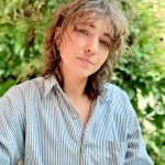 Beth Wittmann posing for a headshot with sunlit green foliage in the background