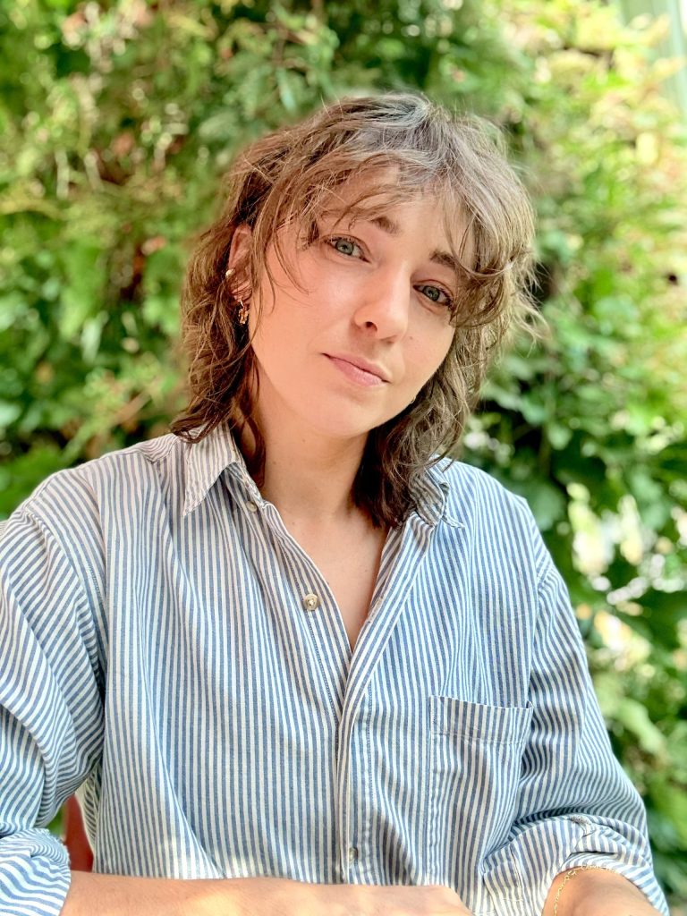Beth Wittmann posing for a headshot with sunlit green foliage in the background