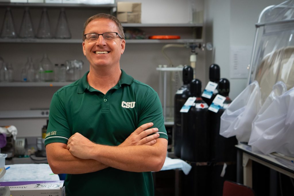 Dr. Thomas Santangelo stands in a lab with arms crossed and smiling at the camera while wearing a CSU green polo shirt.