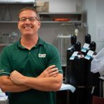 Dr. Thomas Santangelo stands in a lab with arms crossed and smiling at the camera while wearing a CSU green polo shirt.