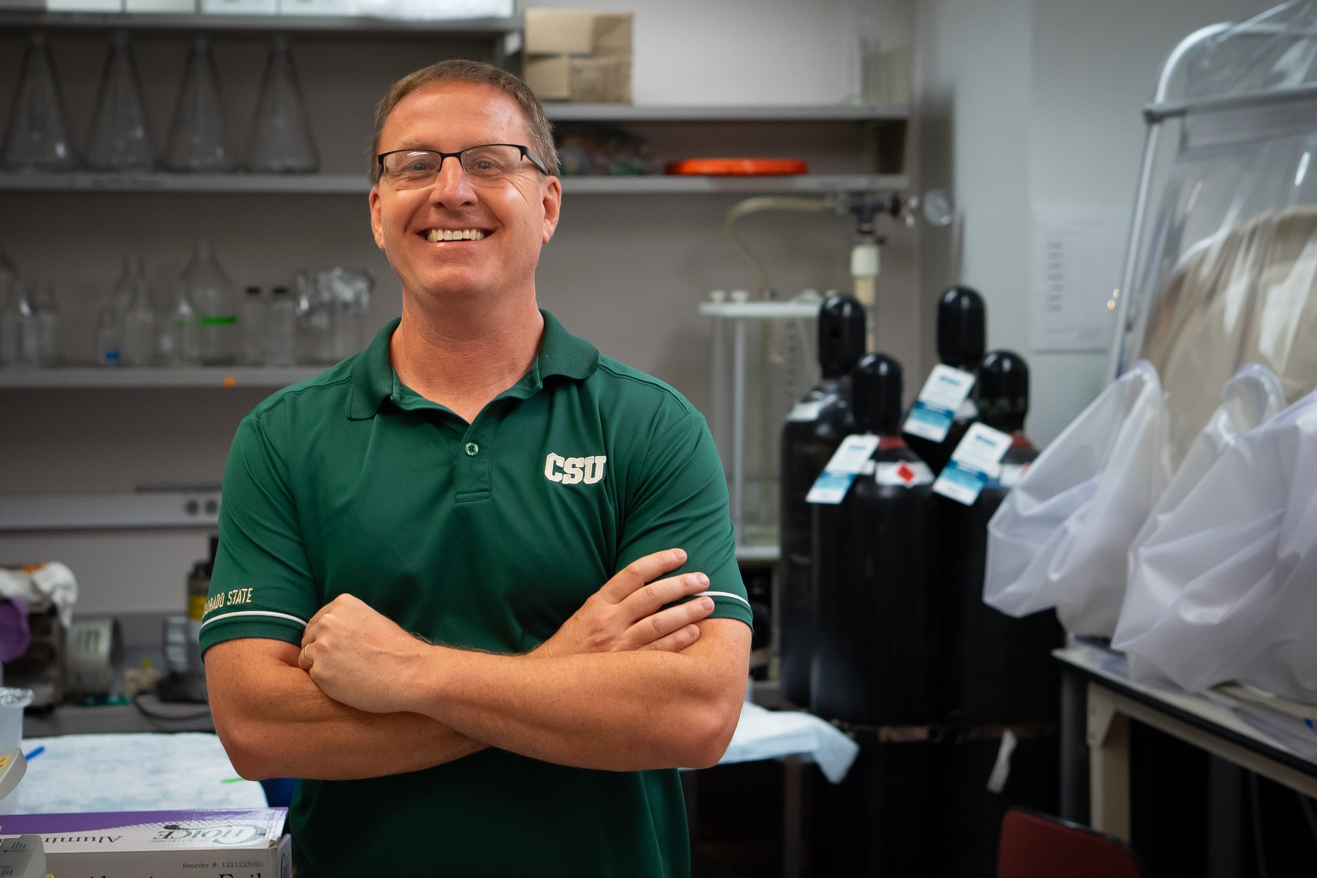 Dr. Thomas Santangelo stands in a lab with arms crossed and smiling at the camera while wearing a CSU green polo shirt.