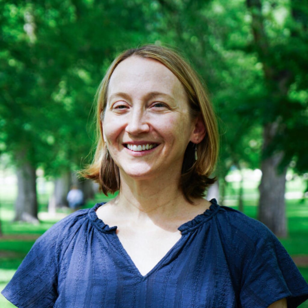Dr. Jennifer Boyd stands amidst lush green sun dappled trees on the CSU campus while smiling warmly for her portrait. She wears a blue blouse with her hair down and cut short above the shoulders.