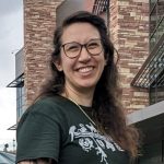 mecam2023 Woman with brown hair and glasses wearing green shirt with white animal logo