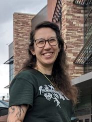 Woman with brown hair and glasses wearing green shirt with white animal logo